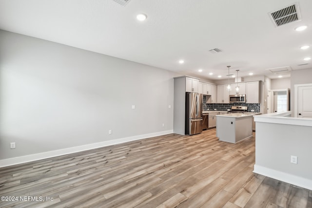 kitchen featuring hanging light fixtures, stainless steel appliances, tasteful backsplash, a kitchen island, and light wood-type flooring