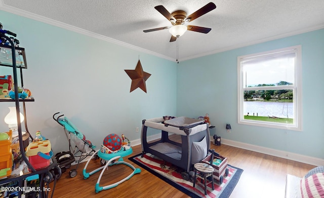 playroom featuring a textured ceiling, ceiling fan, crown molding, and light hardwood / wood-style flooring