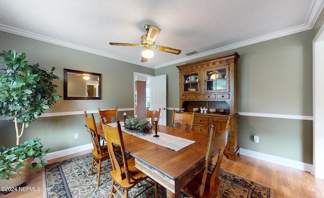 dining space featuring ceiling fan, light wood-type flooring, a textured ceiling, and ornamental molding