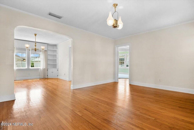 empty room with a healthy amount of sunlight, an inviting chandelier, built in shelves, and light hardwood / wood-style floors