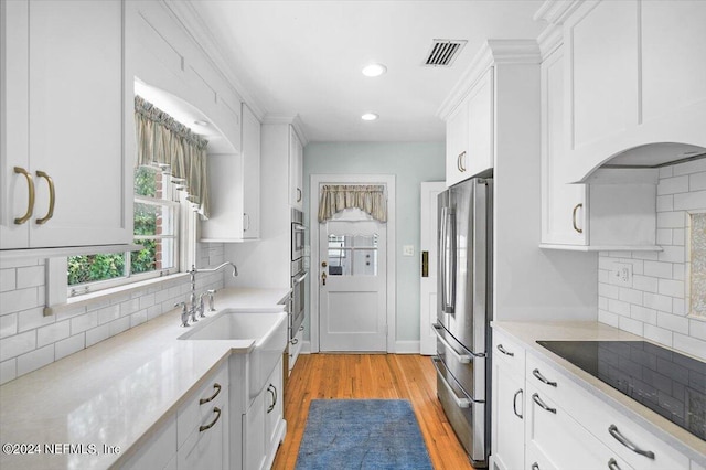 kitchen with light wood-type flooring, tasteful backsplash, white cabinetry, and appliances with stainless steel finishes