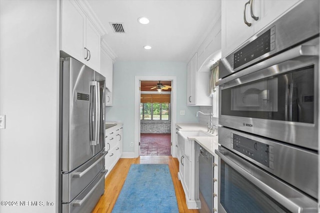 kitchen with stainless steel appliances, ceiling fan, white cabinetry, light wood-type flooring, and sink