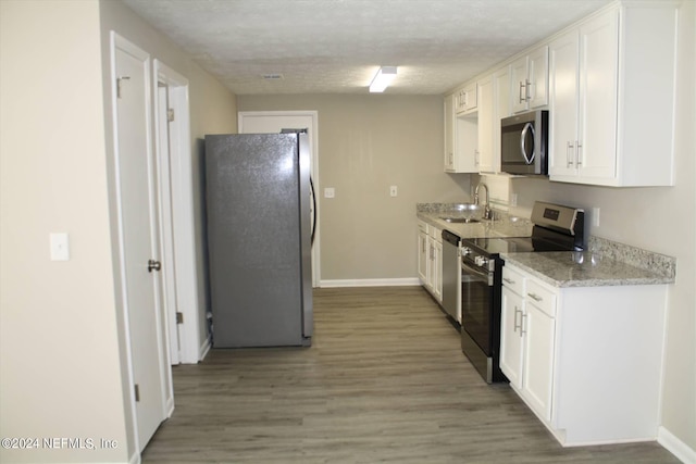 kitchen with light stone counters, hardwood / wood-style floors, white cabinetry, appliances with stainless steel finishes, and sink