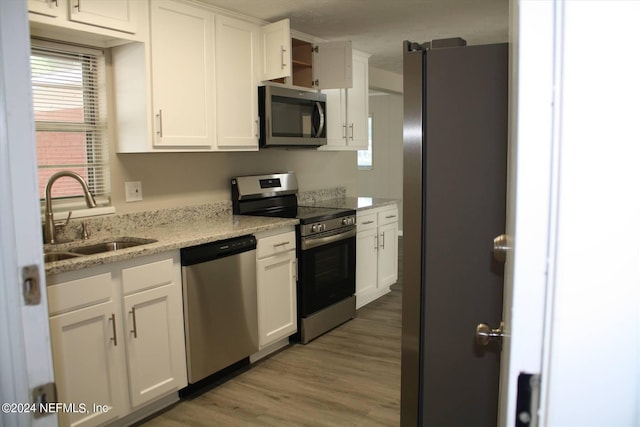 kitchen featuring light stone counters, hardwood / wood-style flooring, white cabinetry, appliances with stainless steel finishes, and sink