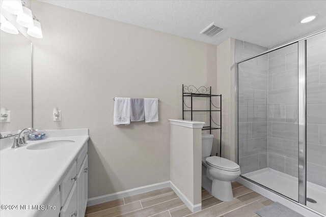 bathroom with a shower with door, vanity, a textured ceiling, and toilet