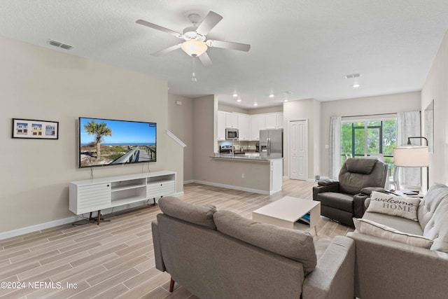 living room featuring ceiling fan, light hardwood / wood-style flooring, and a textured ceiling