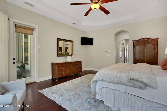 bedroom with dark wood-style floors, baseboards, a raised ceiling, visible vents, and arched walkways