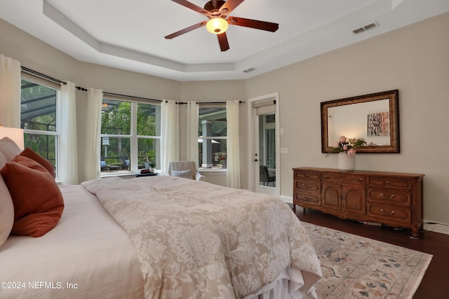 bedroom featuring ceiling fan, visible vents, access to outside, dark wood-type flooring, and a tray ceiling