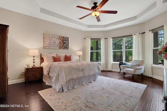 bedroom with baseboards, a tray ceiling, a ceiling fan, and dark wood finished floors