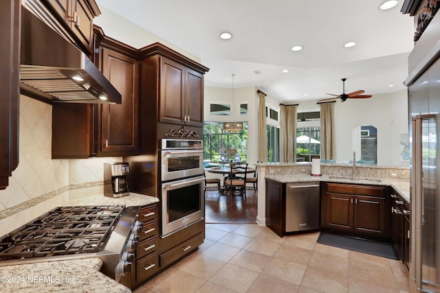 kitchen with hanging light fixtures, light stone counters, a sink, ventilation hood, and stainless steel appliances