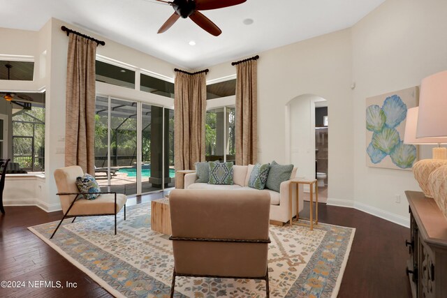 living area with ceiling fan, baseboards, arched walkways, a sunroom, and dark wood-type flooring