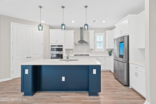 kitchen featuring a center island with sink, white cabinetry, wall chimney range hood, and stainless steel appliances