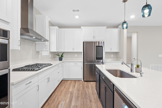 kitchen with sink, white cabinets, stainless steel appliances, and wall chimney range hood