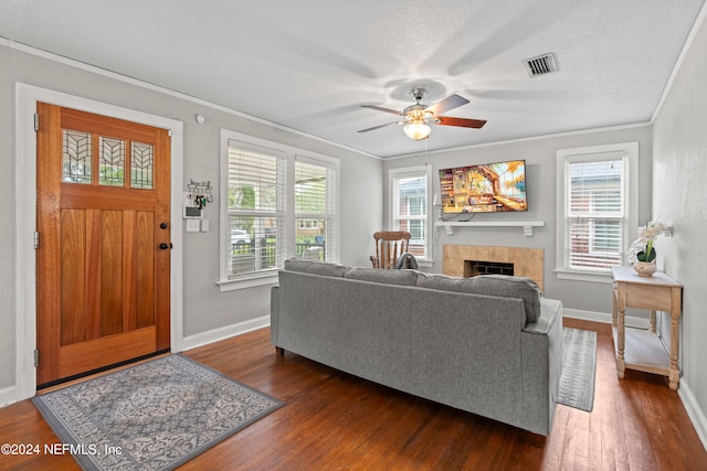 living room with dark hardwood / wood-style floors, ceiling fan, ornamental molding, a tile fireplace, and a textured ceiling