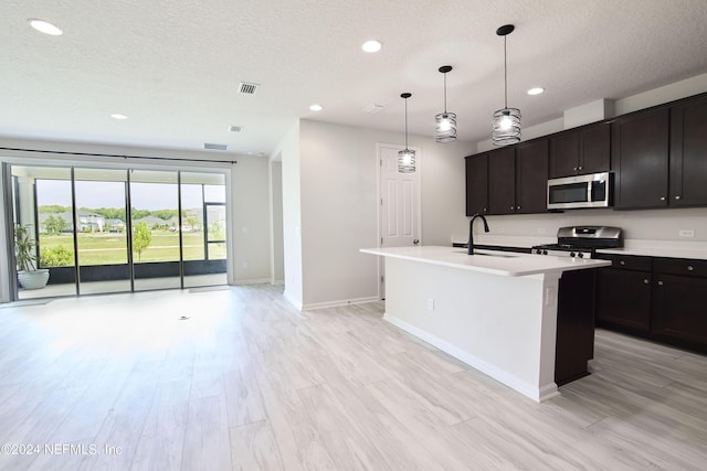 kitchen with sink, dark brown cabinets, appliances with stainless steel finishes, an island with sink, and light hardwood / wood-style floors