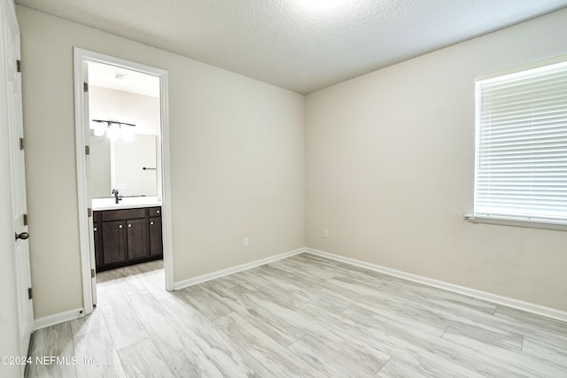 unfurnished bedroom featuring multiple windows, ensuite bath, a textured ceiling, and light hardwood / wood-style flooring