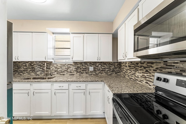 kitchen with sink, decorative backsplash, range with electric stovetop, light stone counters, and white cabinetry