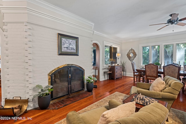 living room featuring brick wall, ornamental molding, dark wood-type flooring, a brick fireplace, and ceiling fan