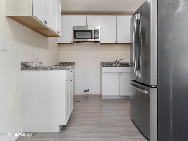 kitchen with stainless steel appliances, white cabinetry, and light hardwood / wood-style floors