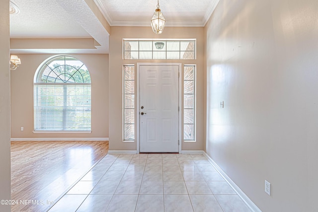 tiled foyer entrance with crown molding, a textured ceiling, and a notable chandelier