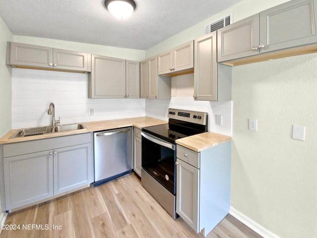 kitchen with appliances with stainless steel finishes, sink, light hardwood / wood-style flooring, and a textured ceiling