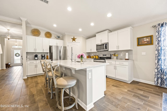 kitchen featuring stainless steel appliances, tasteful backsplash, white cabinets, and a center island with sink