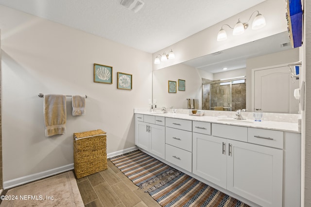 bathroom with a shower with door, a textured ceiling, and dual bowl vanity