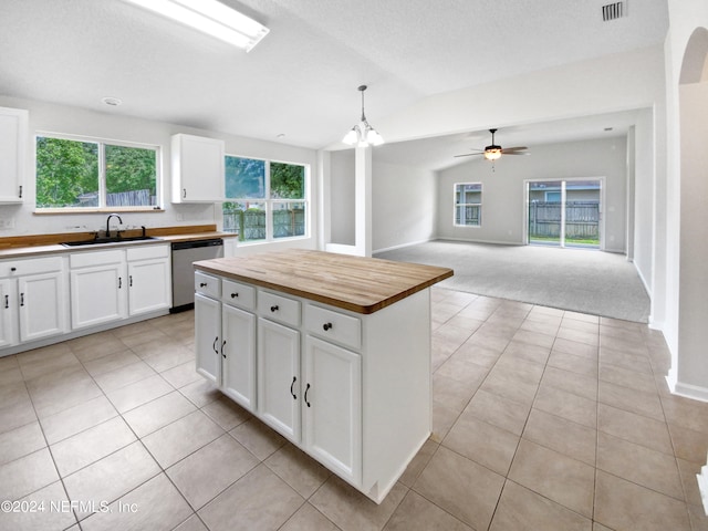 kitchen featuring stainless steel dishwasher, decorative light fixtures, wooden counters, light tile floors, and a center island