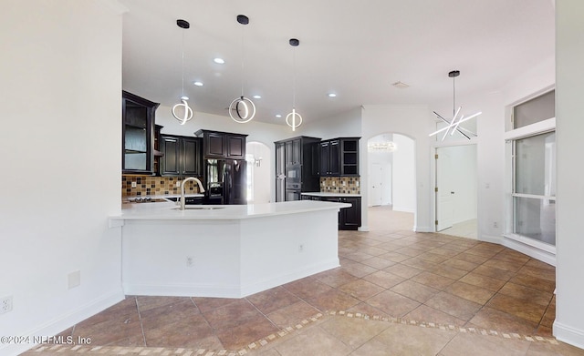 kitchen featuring tasteful backsplash, black refrigerator with ice dispenser, sink, pendant lighting, and an inviting chandelier