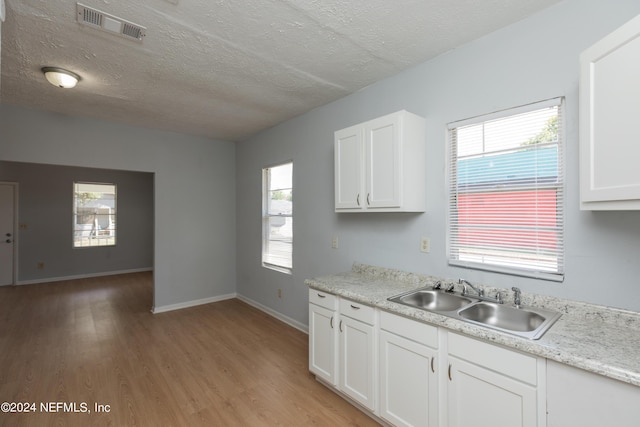 kitchen with light wood finished floors, a sink, visible vents, and white cabinetry