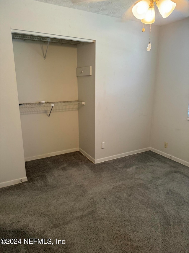 unfurnished bedroom with dark colored carpet, ceiling fan, and a closet