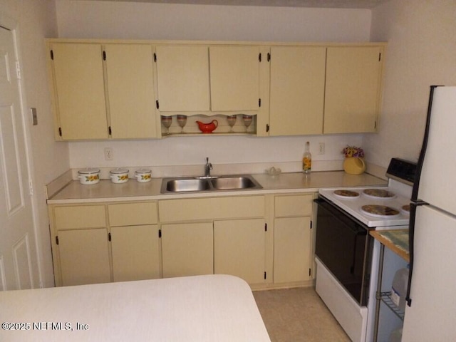 kitchen featuring range with electric cooktop, white fridge, sink, and cream cabinets