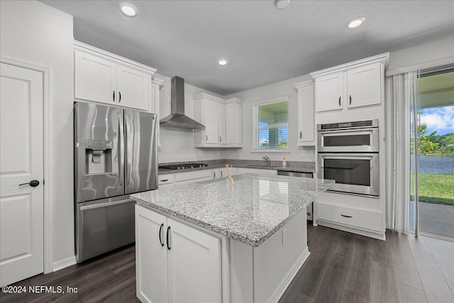 kitchen with white cabinets, appliances with stainless steel finishes, wall chimney exhaust hood, and dark hardwood / wood-style floors