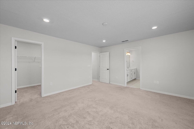 unfurnished bedroom with a textured ceiling, light carpet, connected bathroom, a spacious closet, and a closet