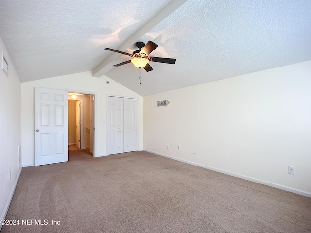 unfurnished bedroom featuring ceiling fan, vaulted ceiling with beams, carpet floors, a textured ceiling, and a closet