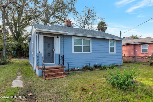 bungalow-style house with a chimney, a shingled roof, entry steps, a front yard, and fence