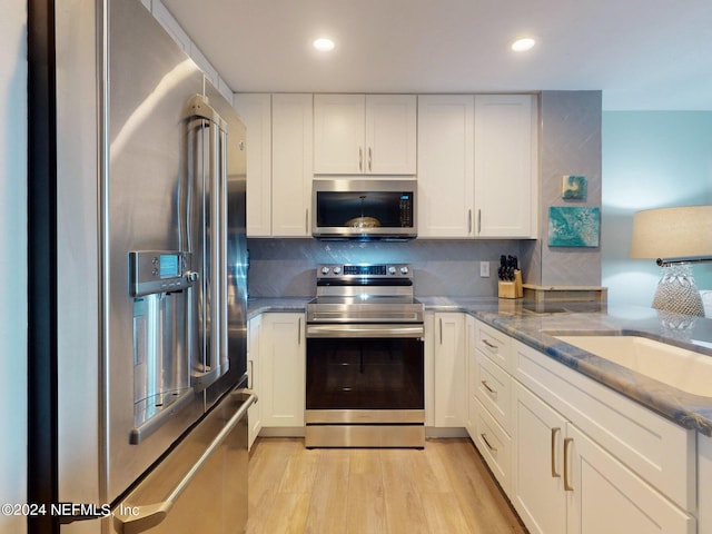 kitchen featuring light hardwood / wood-style flooring, stainless steel appliances, white cabinets, light stone counters, and tasteful backsplash