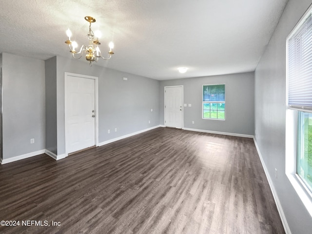 empty room with a textured ceiling, a chandelier, and dark wood-type flooring