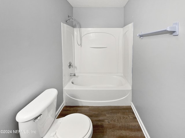 bathroom with washtub / shower combination, wood-type flooring, and toilet