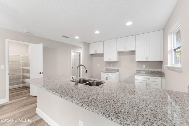 kitchen featuring sink, white cabinets, light wood-type flooring, and light stone counters