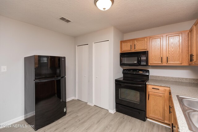 kitchen with sink, black appliances, a textured ceiling, and light hardwood / wood-style floors