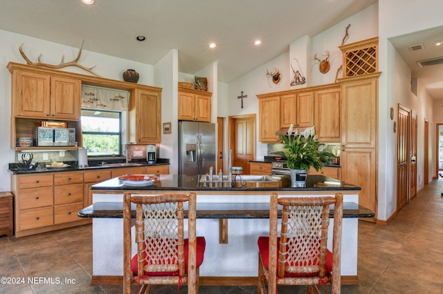 kitchen with high vaulted ceiling, a kitchen bar, a center island with sink, dark tile patterned flooring, and appliances with stainless steel finishes