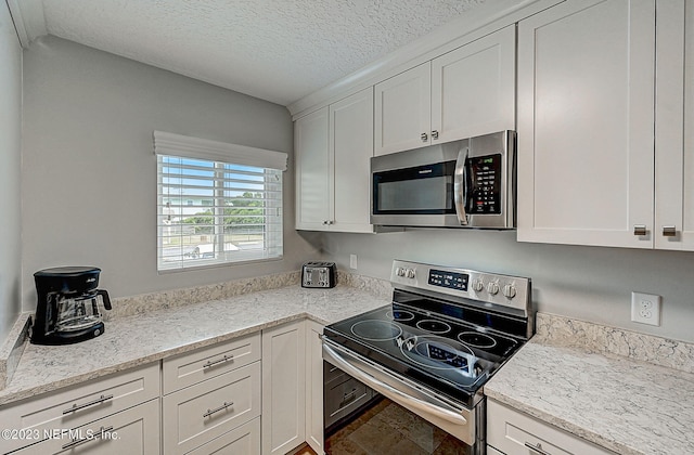 8550 A1A Unit 12122, Saint Augustine, FL 32080 - kitchen featuring a textured ceiling, light stone counters, white cabinets, and appliances with stainless steel finishes