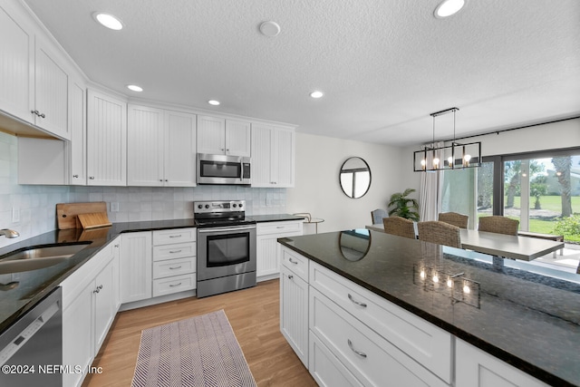 kitchen with light hardwood / wood-style flooring, white cabinets, decorative light fixtures, and appliances with stainless steel finishes