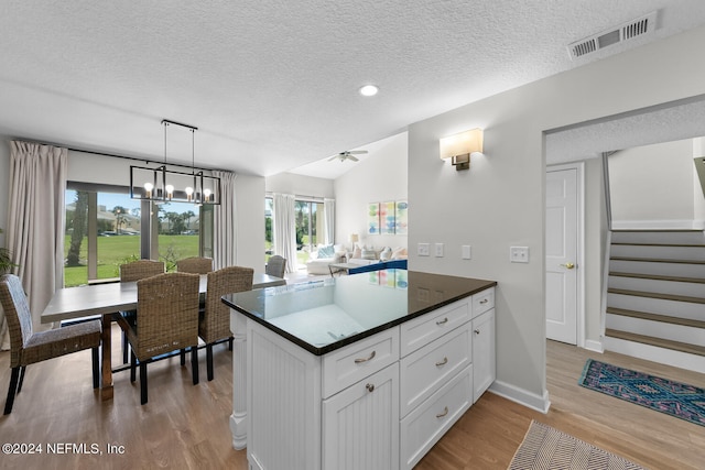 kitchen with pendant lighting, lofted ceiling, white cabinetry, and light hardwood / wood-style flooring