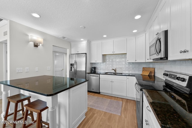 kitchen with white cabinets, light wood-type flooring, tasteful backsplash, a kitchen bar, and stainless steel appliances