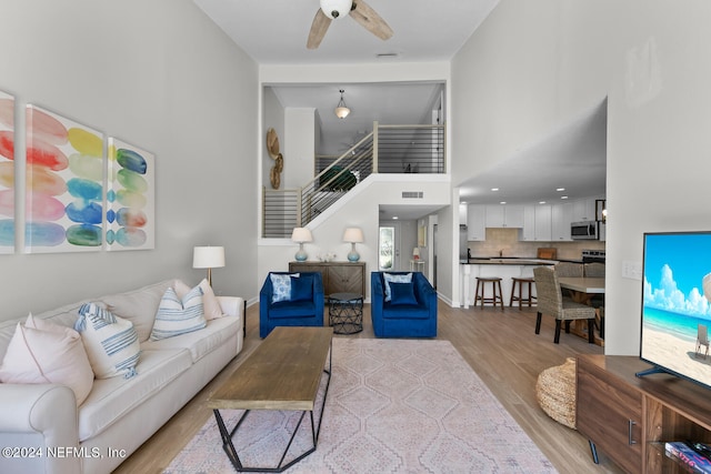 living room featuring a high ceiling, light hardwood / wood-style flooring, and ceiling fan