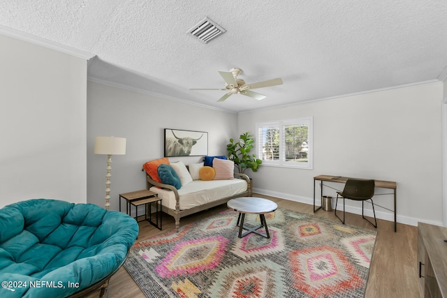 living room with ceiling fan, crown molding, light wood-type flooring, and a textured ceiling