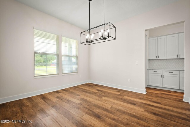 unfurnished dining area with wood-type flooring and an inviting chandelier