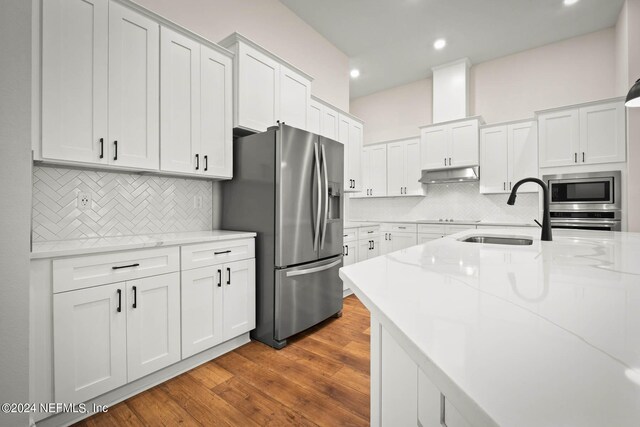 kitchen featuring tasteful backsplash, wood-type flooring, sink, white cabinets, and appliances with stainless steel finishes